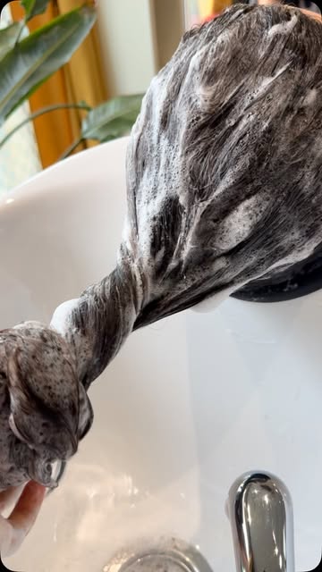 Lavage de cheveux avec shampoing moussant dans un bac de salon de coiffure professionnel.